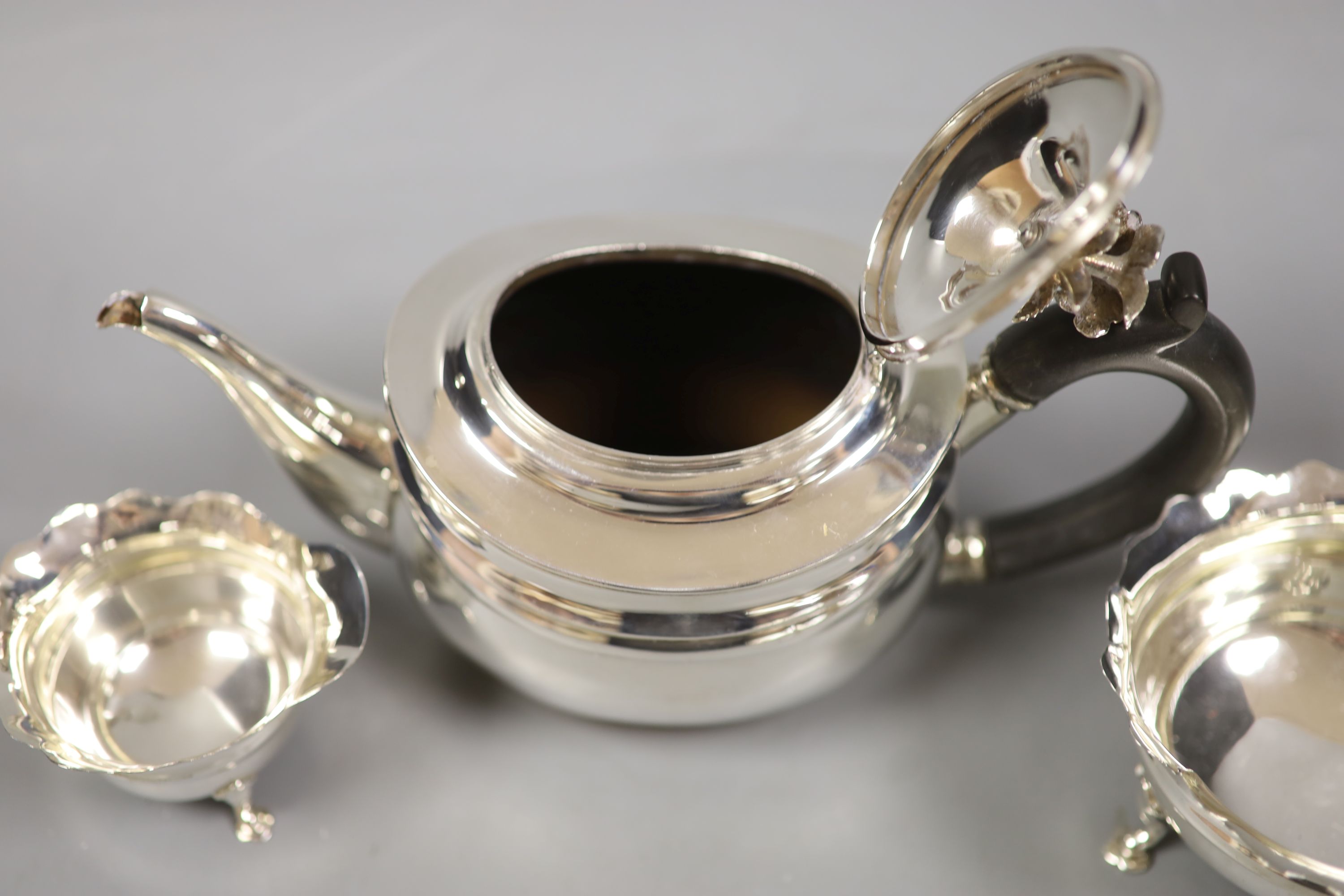 A George V silver teapot with floral finial, London, 1927 together with an associated cream jug, Chester 1907 and an Art Deco silver small dish